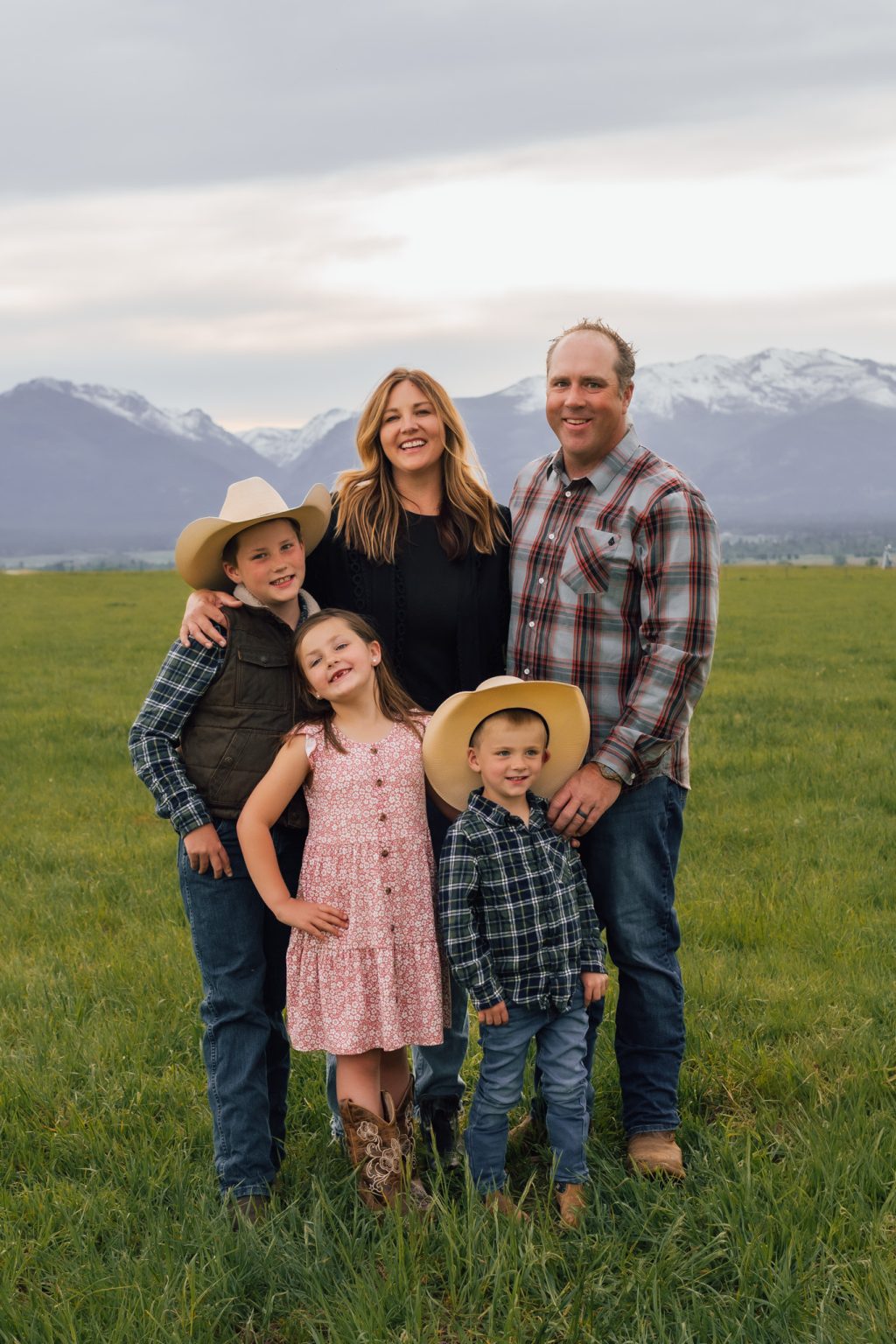 The Mouw family standing in a Montana field with mountains and cows in the background.